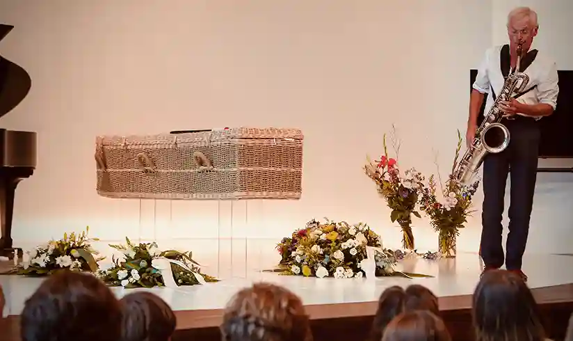 Een podium met daarop een rieten uitvaartkist en een man die saxofoon speelt